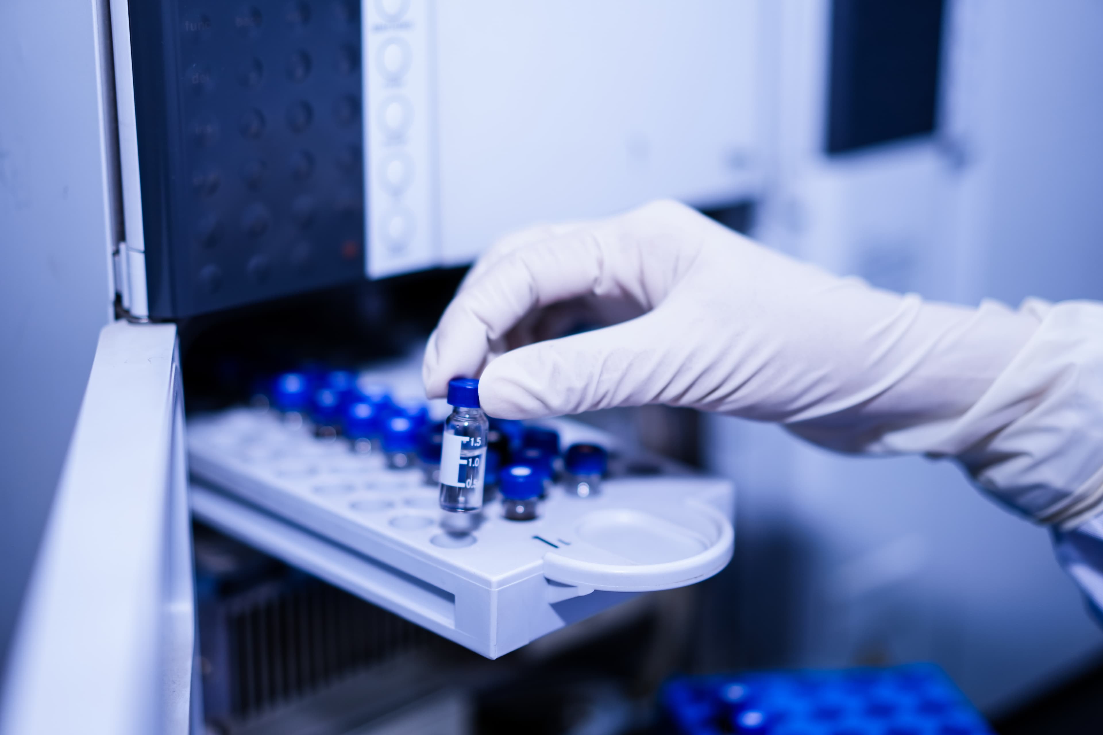 Gloved hand placing a sample vial into laboratory testing equipment